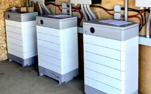 Es una batería de 10kw suficiente para ejecutar una casa apilablelecon íconos que representan sus beneficios claveieun banco de cerdounAhorros An image of a home with a stackable battery, with icons representing its key benefits: a piggy bank (Savings), a shield (Security), and an arrow showing growth (Flexibility).